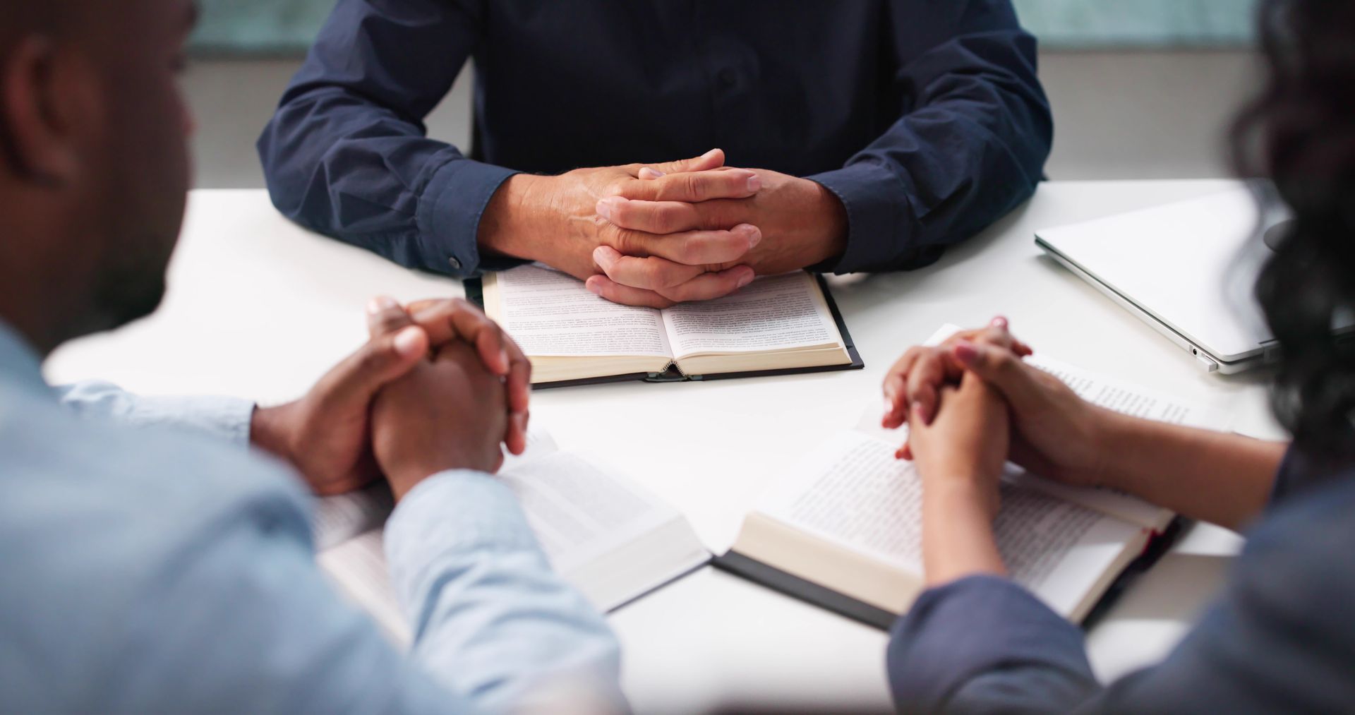 Three people in a meeting with hands clasped around a notebook on a table