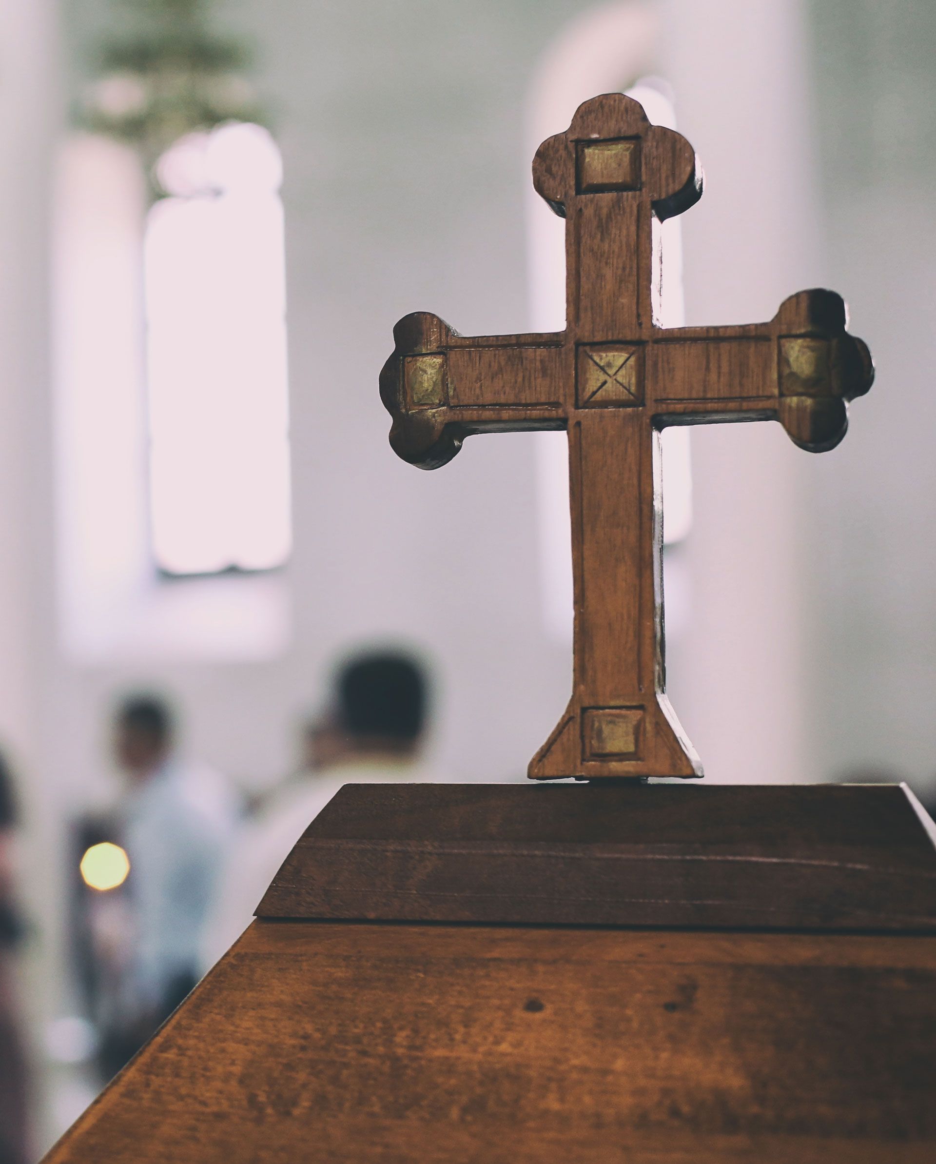 Wooden cross on a church altar with blurred worshippers in the background.