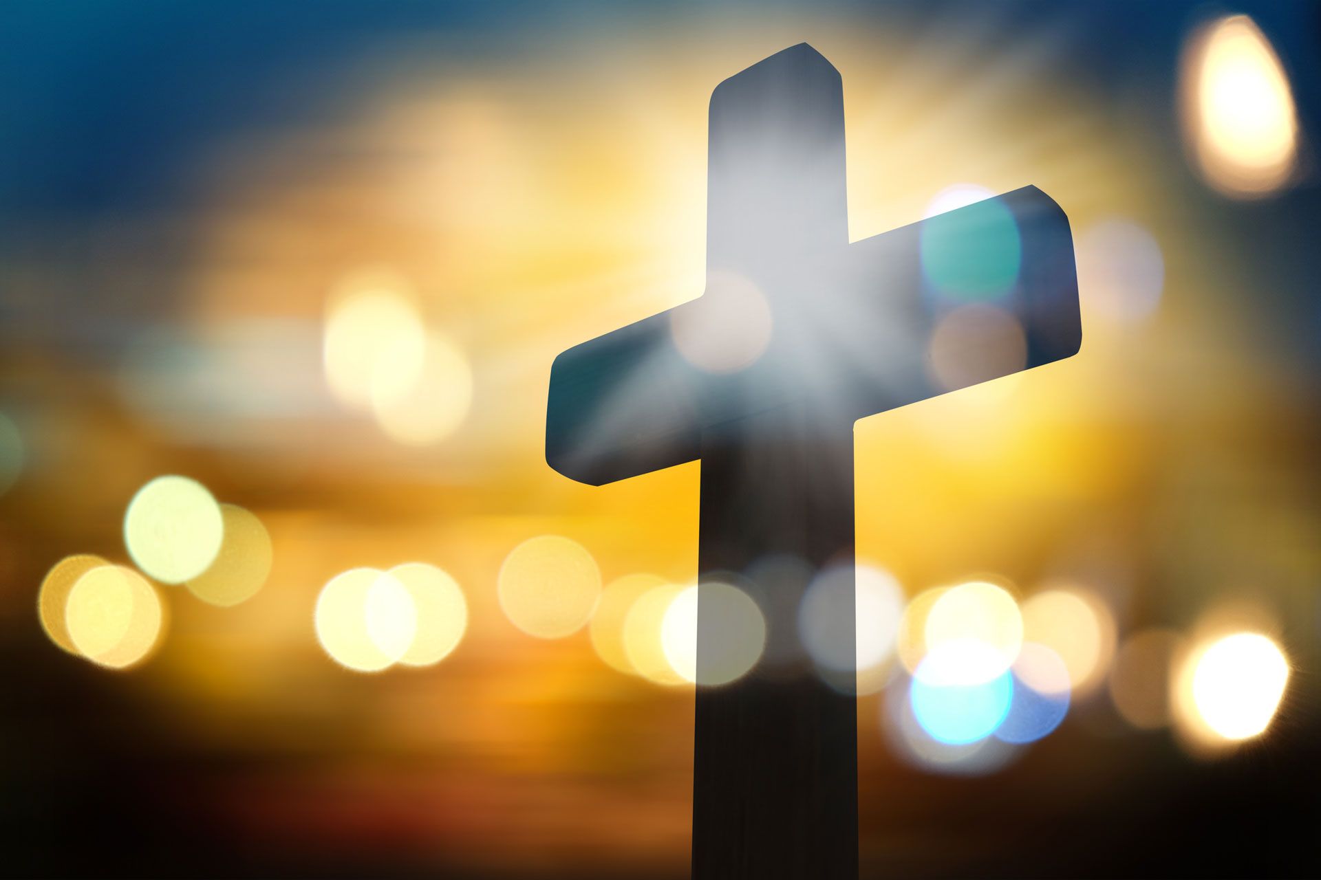 Silhouetted cross against a blurred sunset sky with warm lights in the background