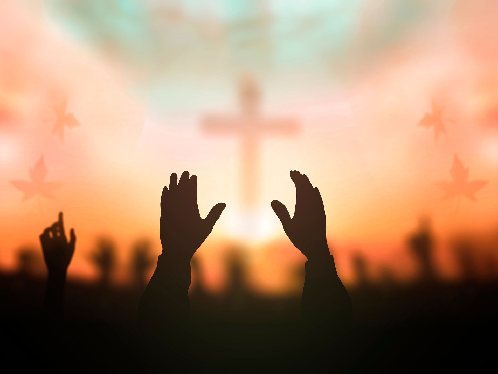 Silhouetted hands raised in worship at sunset, with a blurred cross in the background.