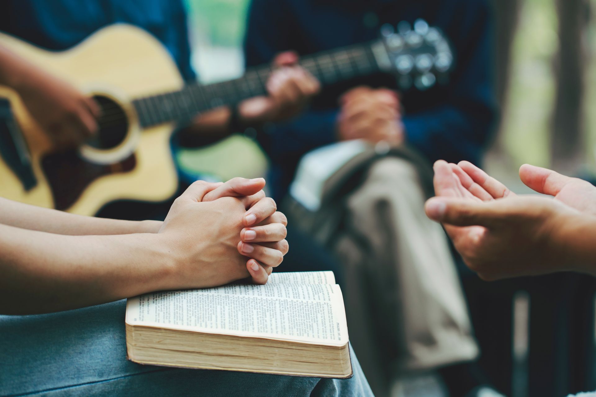 Hands clasped in prayer over an open Bible during a small group worship session