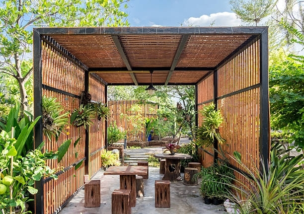 A wooden pergola with tables and chairs in a garden.