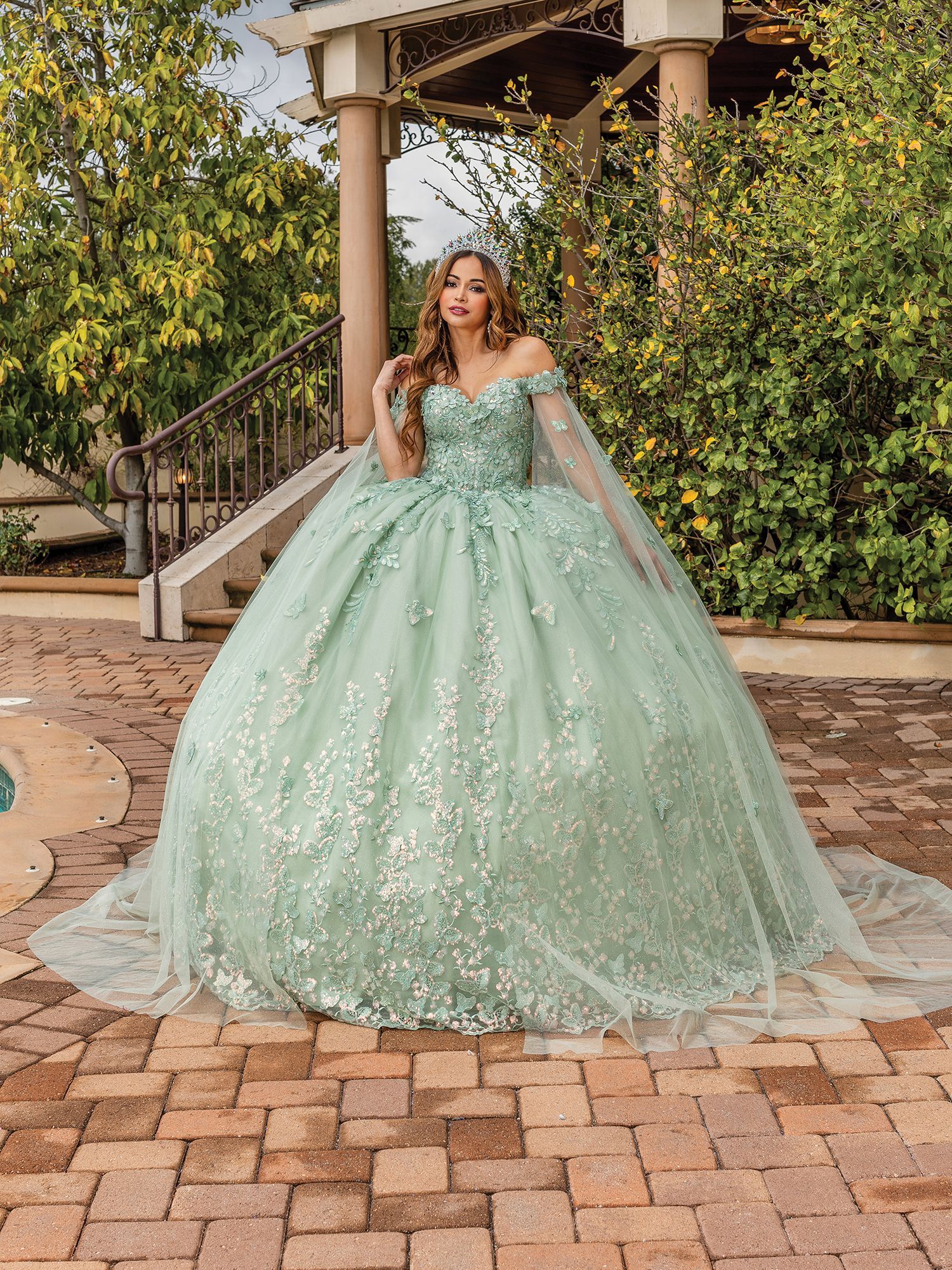 A woman in a green ball gown is standing on a brick sidewalk.