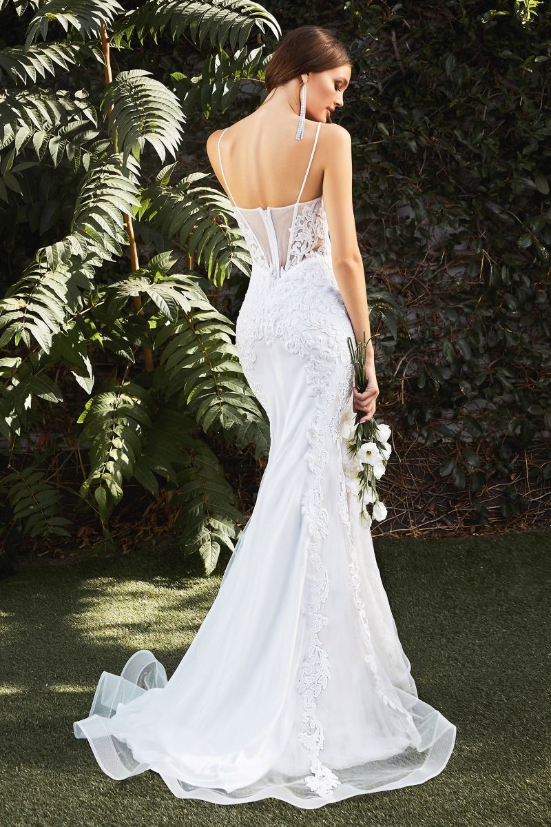 A woman in a white wedding dress is standing in the grass holding a bouquet of flowers.