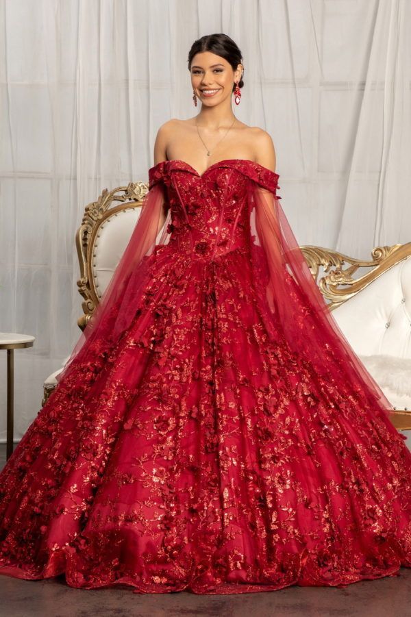 A woman is wearing a red ball gown and standing next to a couch.