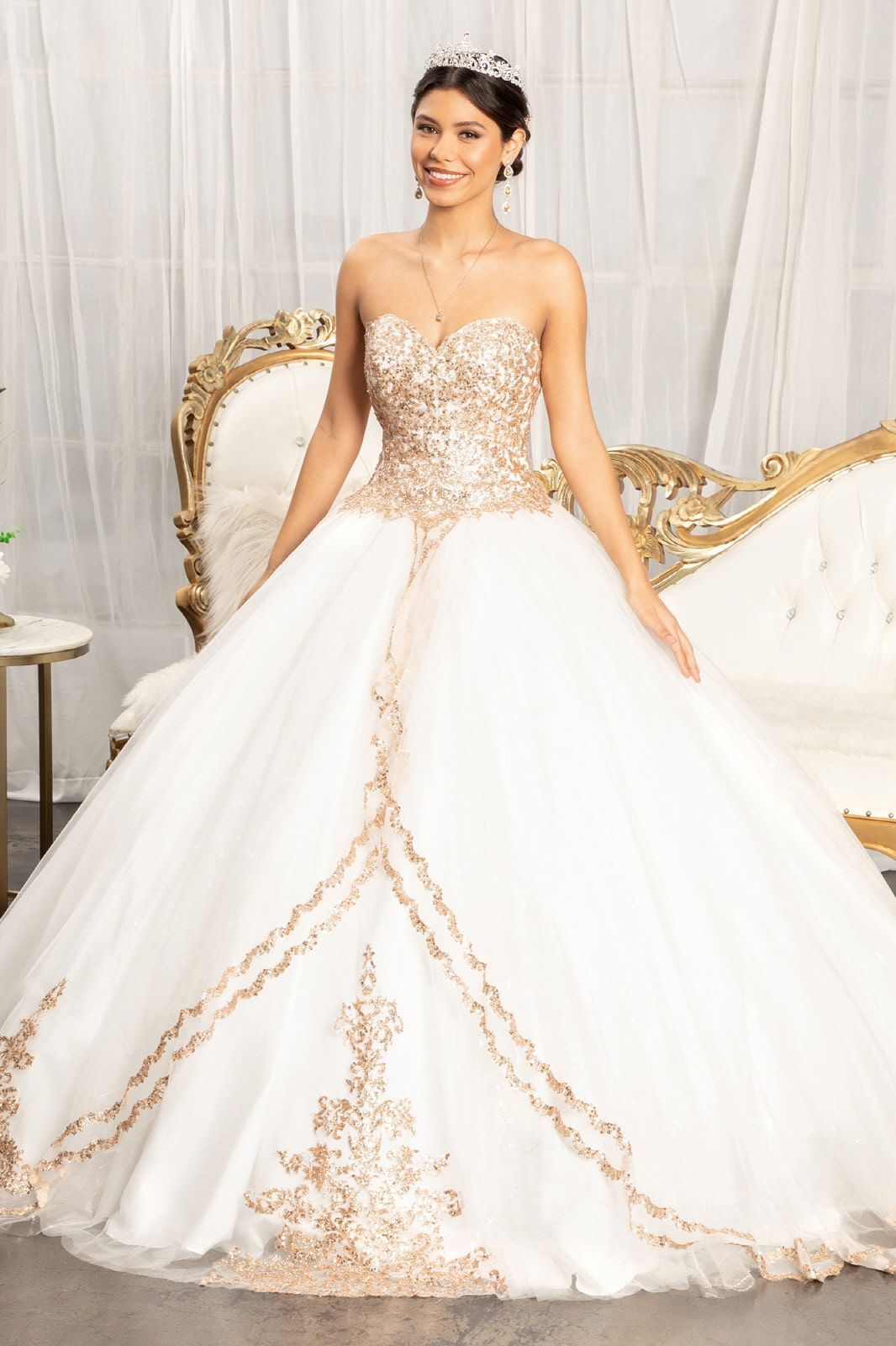 A woman in a white and gold ball gown is standing next to a couch.
