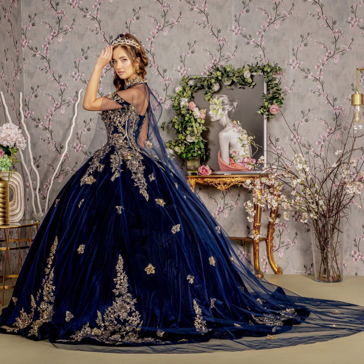 A woman in a blue and gold ball gown is standing in front of a mirror.