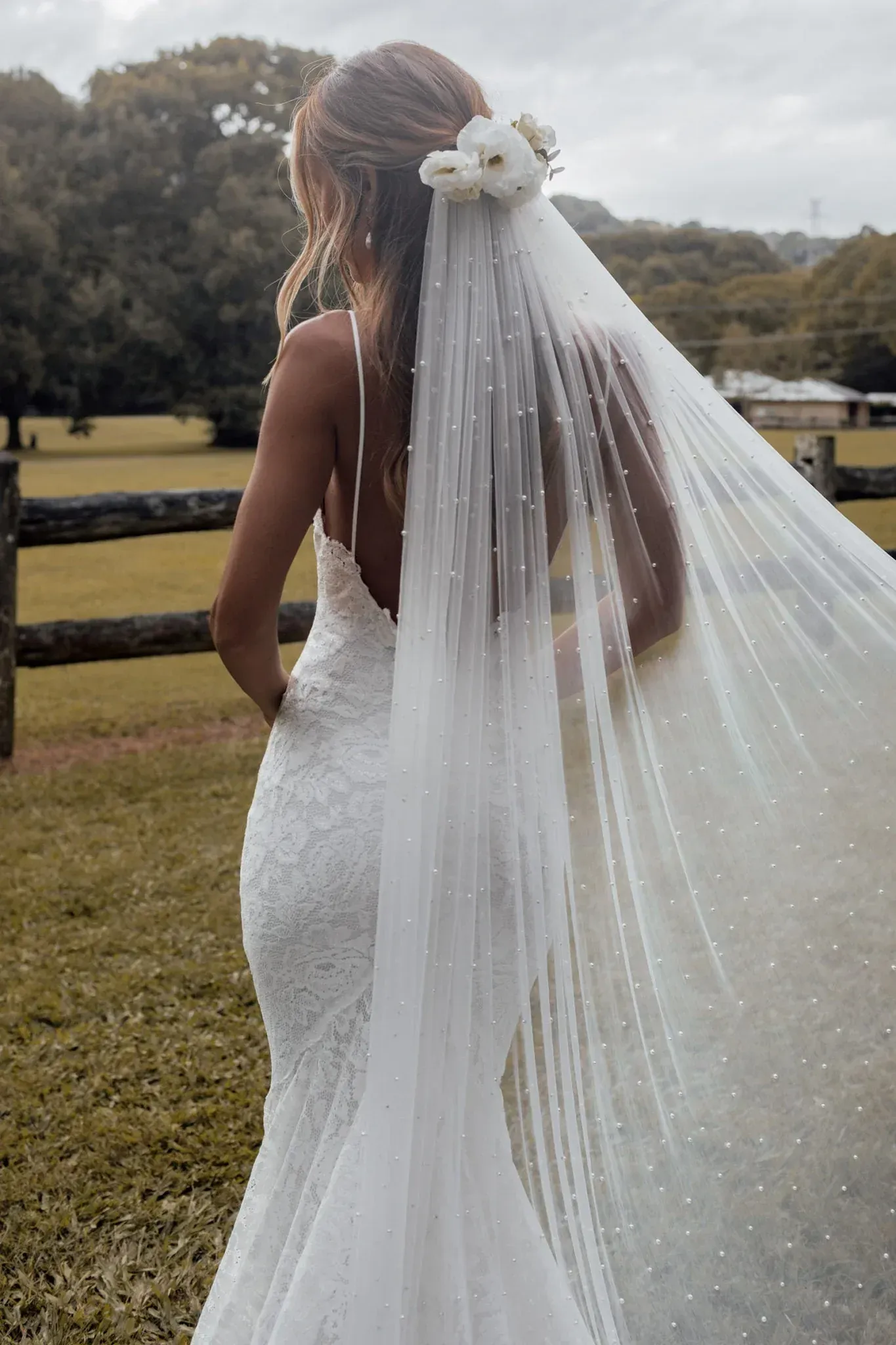 The bride is wearing a long veil and a flower in her hair.