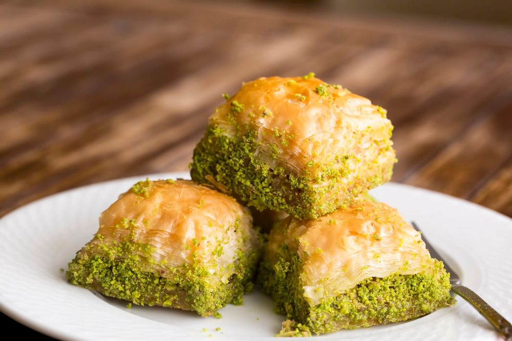 Tre pasticcini ricoperti di pistacchio su un piatto bianco con sfondo di legno.
