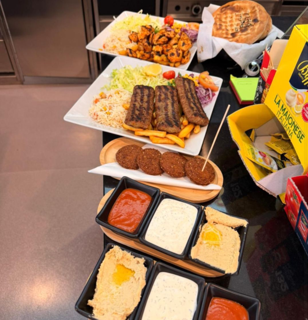 Un assortimento di piatti a buffet su vassoi e piatti, tra cui pasta, pane, salumi, salse e dolci, disposti su un tavolo.