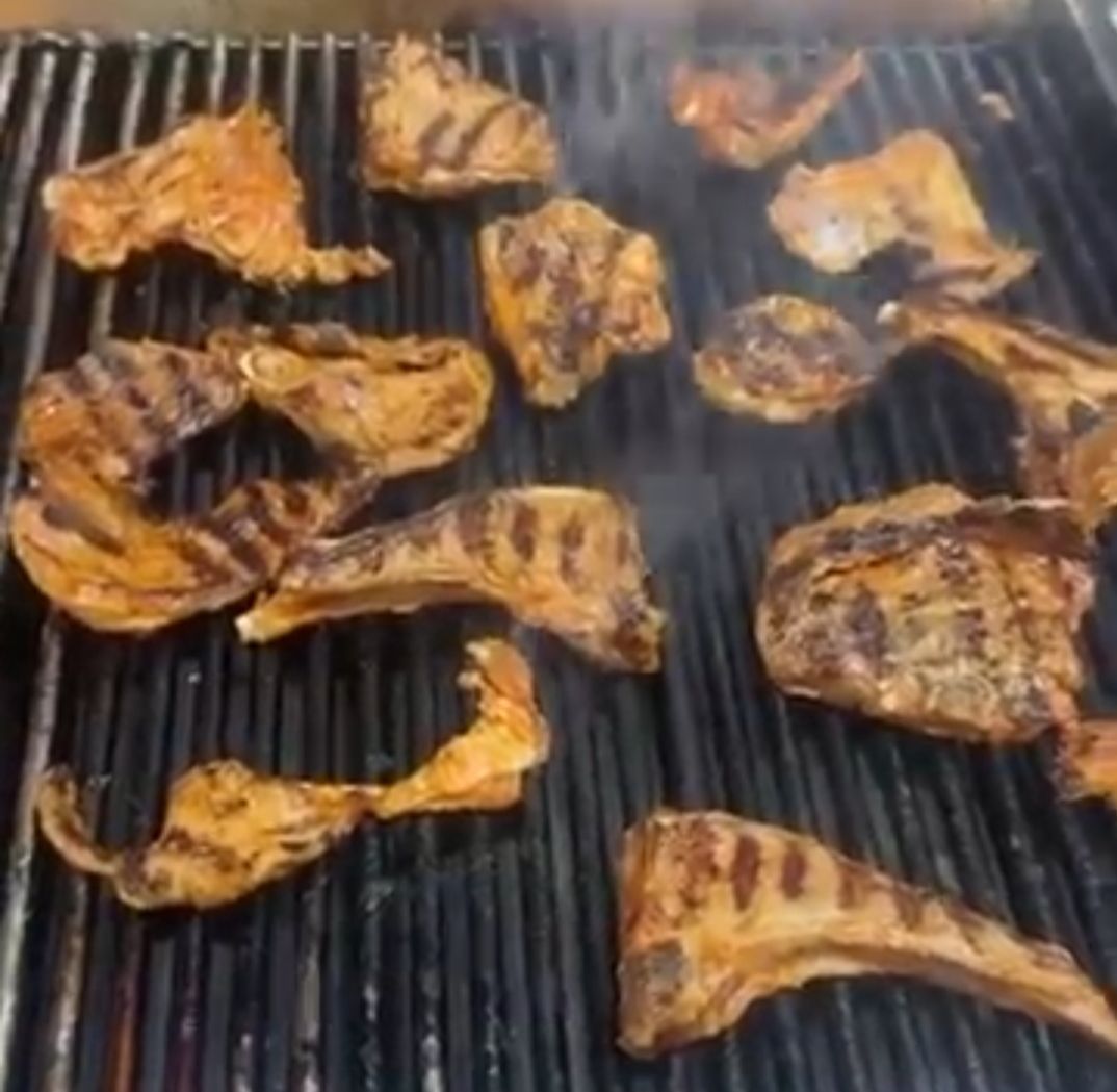 Pezzi di carne marinata grigliati che sfrigolano su una griglia per barbecue scanalata.