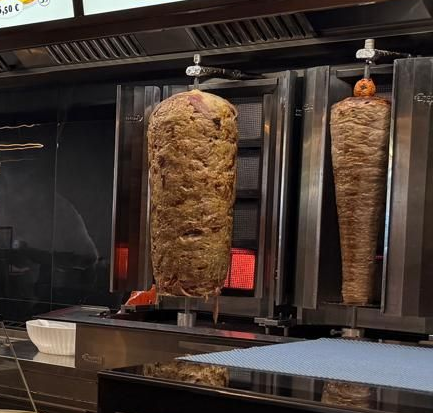 Due spiedi verticali con carne impilata nella cucina di un ristorante, uno sopra braci ardenti