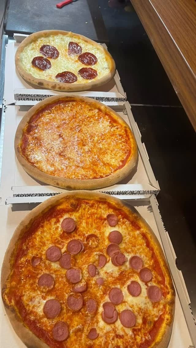 Tre pizze in scatole aperte, tra cui una al salame piccante e una al formaggio, impilate su un bancone.