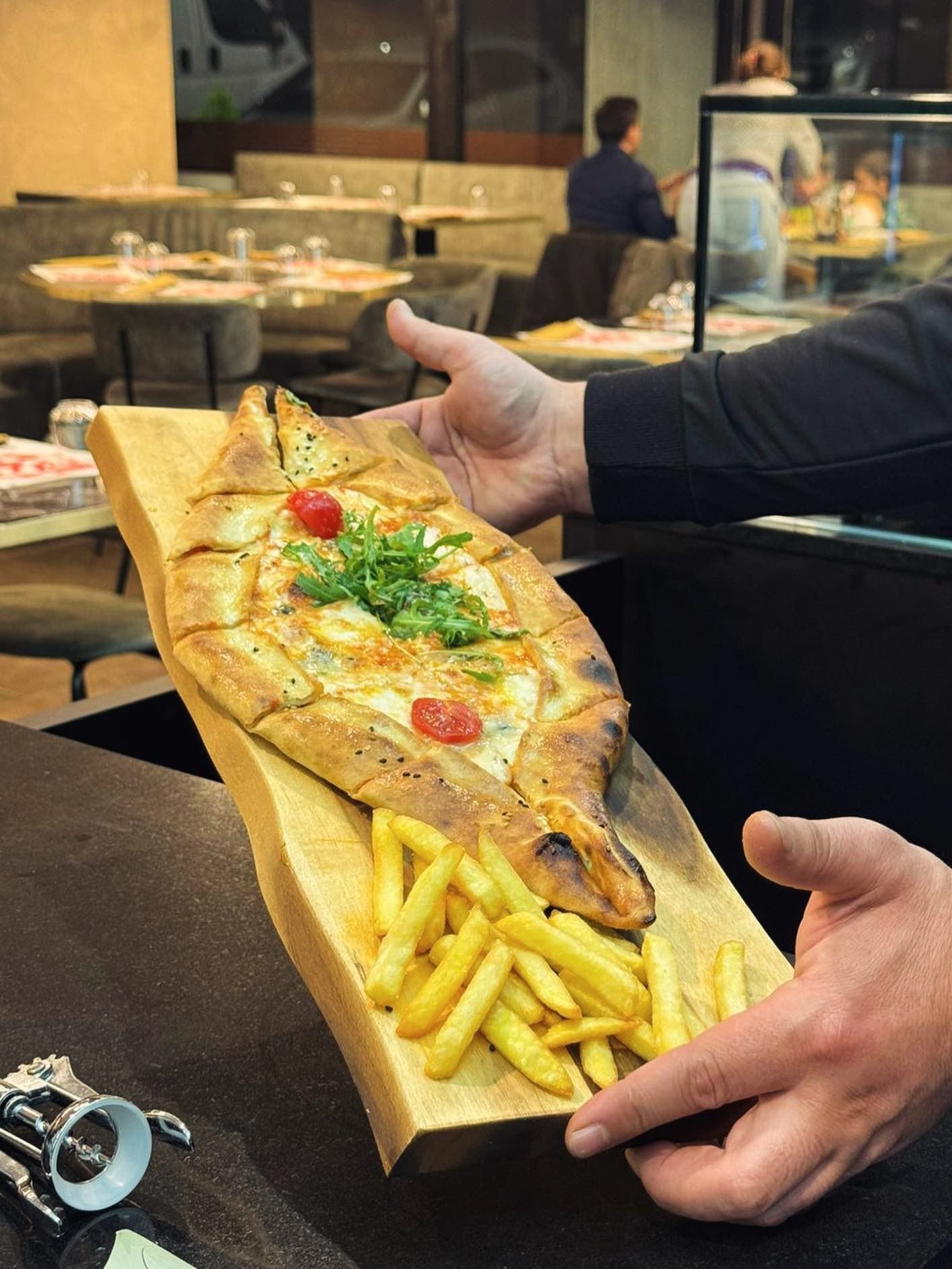 Persona che regge un vassoio di legno con pesce grigliato e patatine fritte in un ristorante