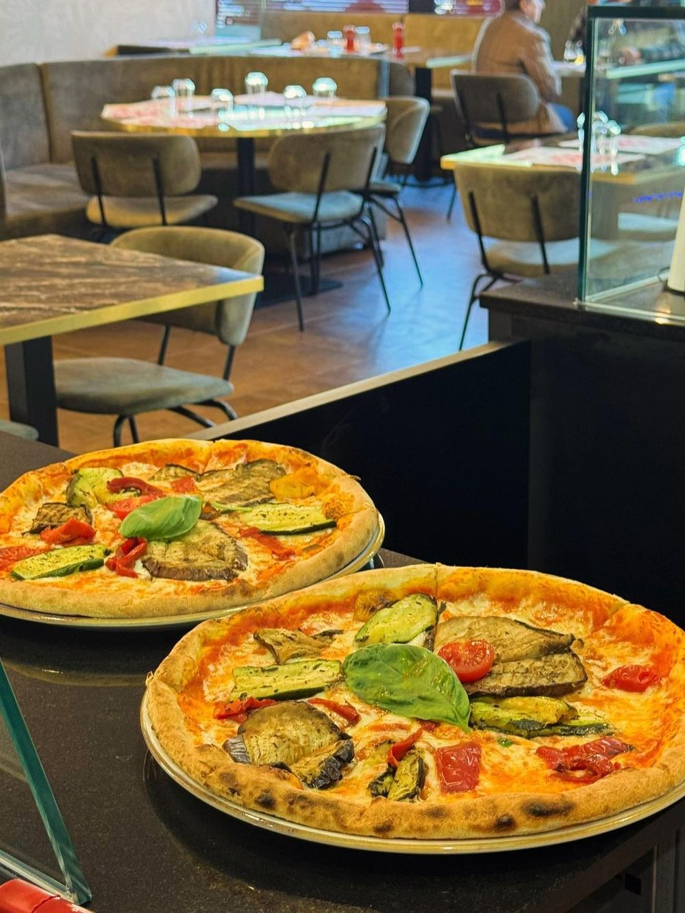 Due pizze su un tavolo in un accogliente ristorante con tavoli e sedie sullo sfondo.