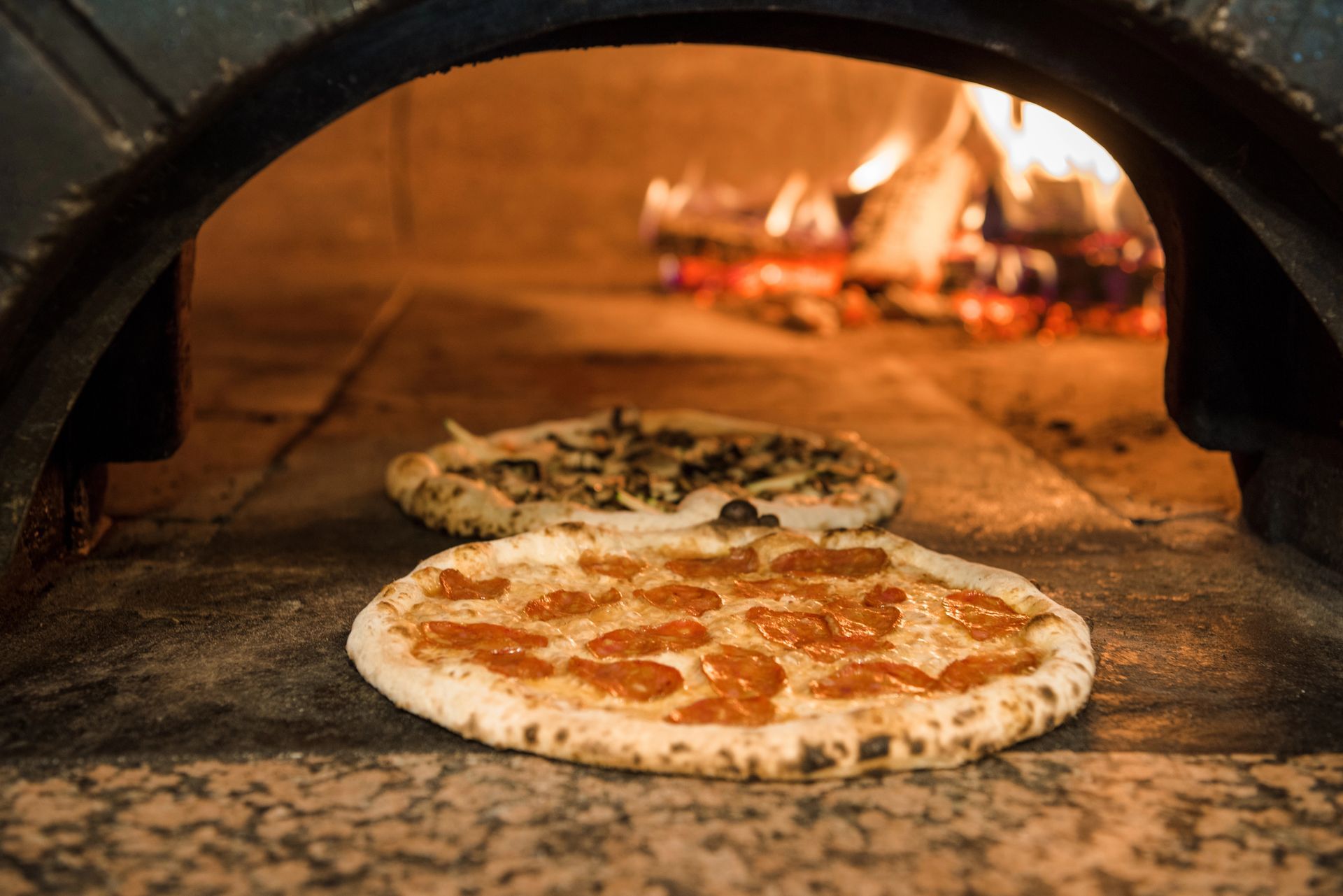 Due pizze che cuociono in un forno a legna, una con i peperoni davanti e una dietro