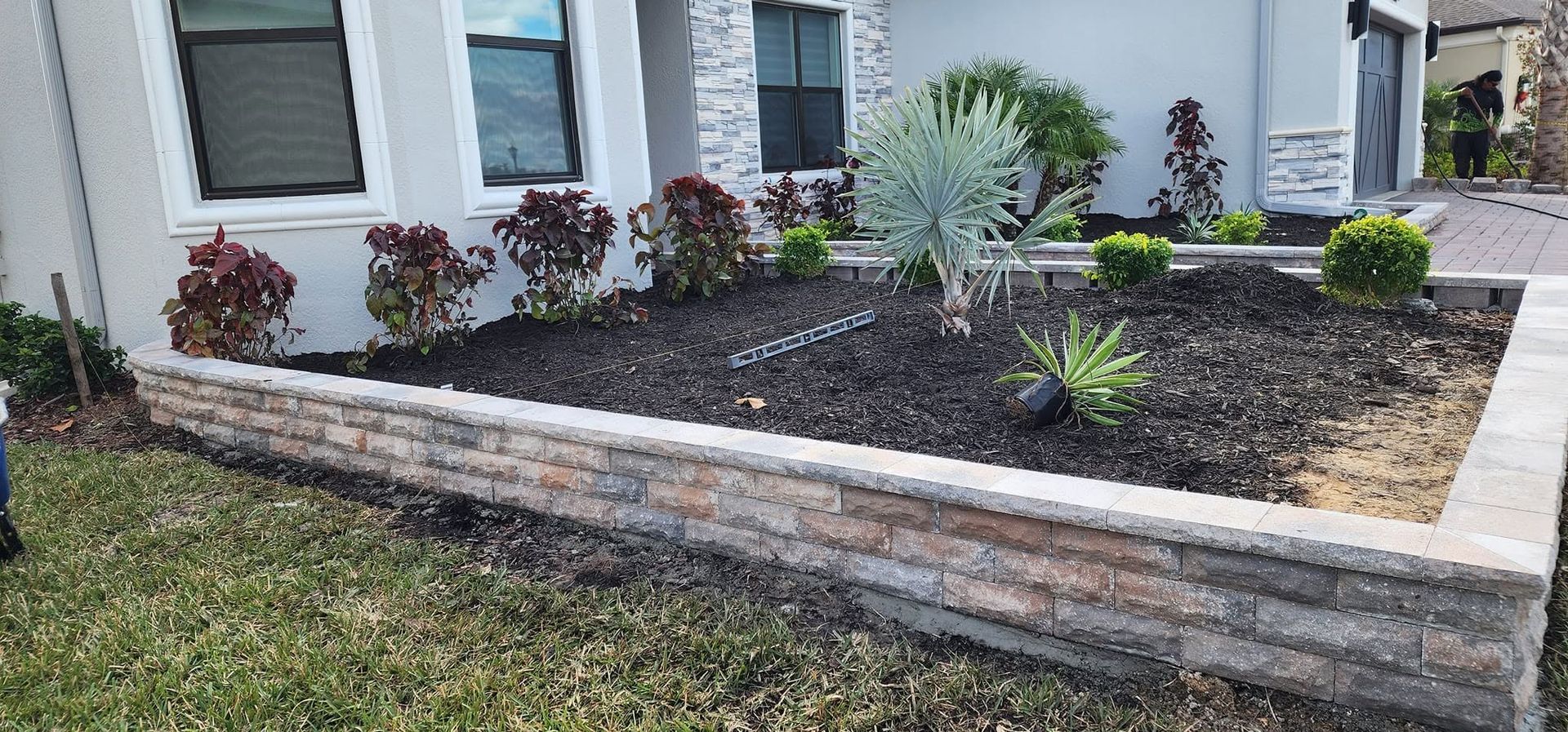 Front yard raised stone planter with mulch, succulents, and shrubs beside a house exterior.