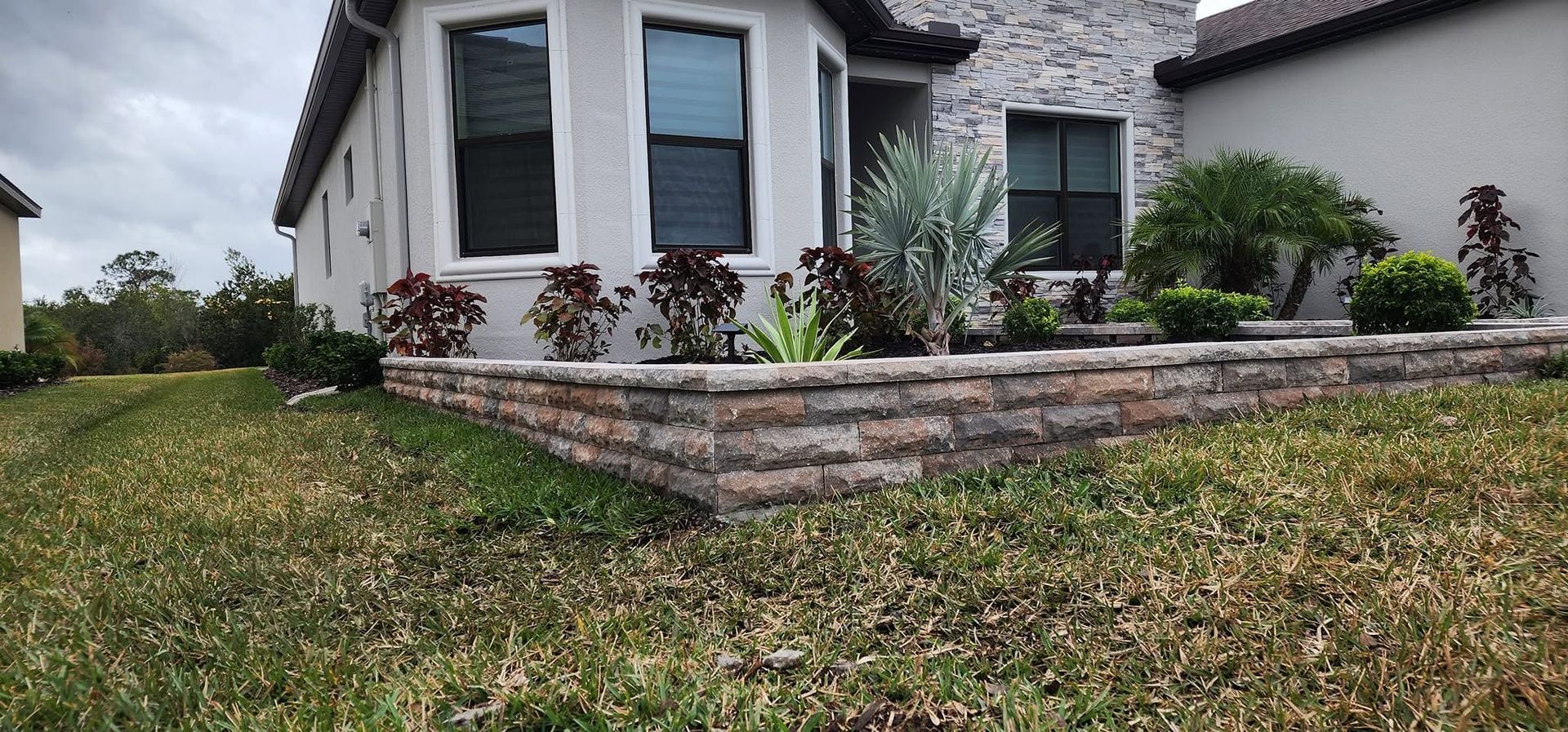 Landscaped suburban house with stone retaining wall and trimmed lawn under cloudy sky