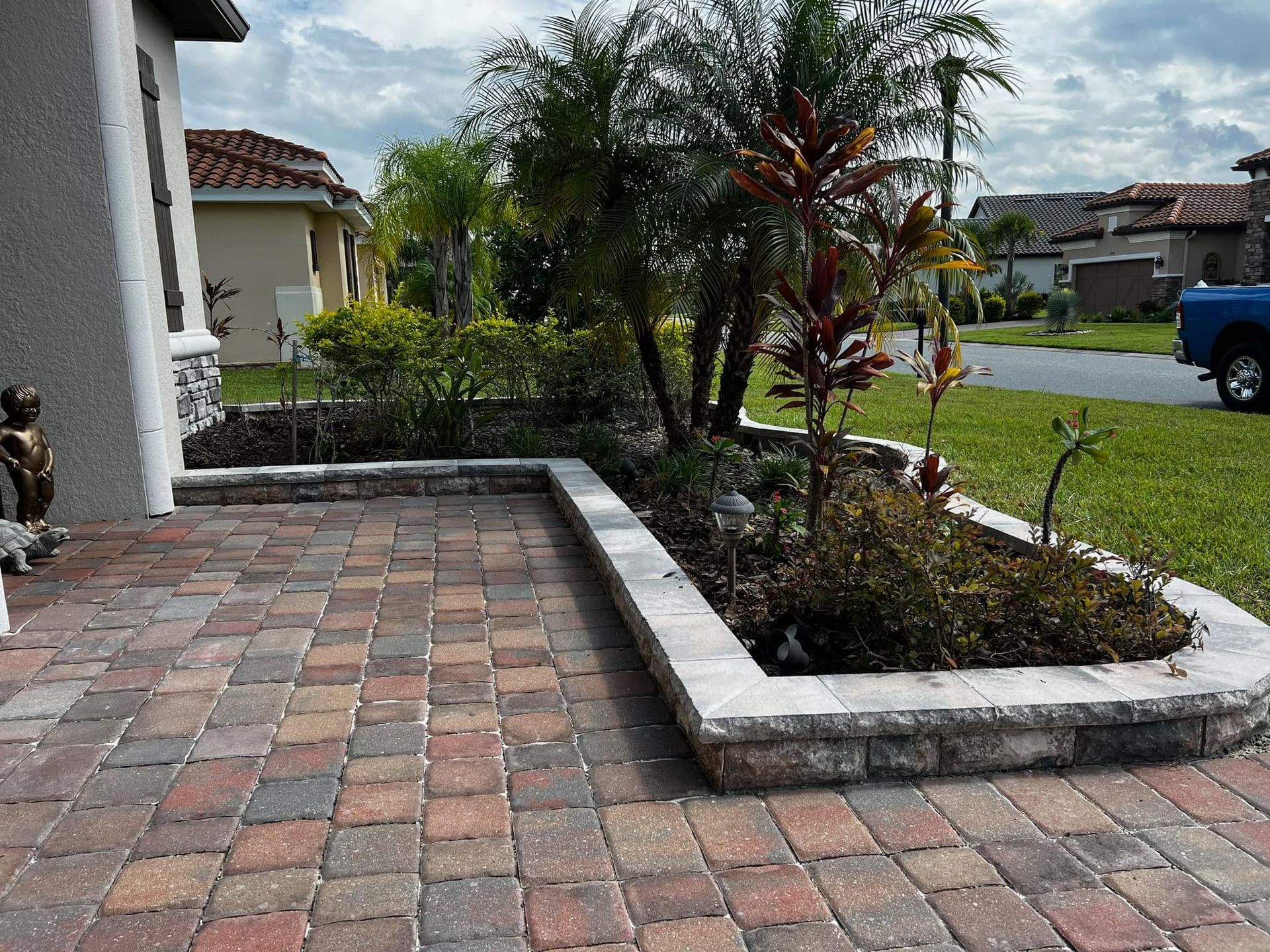 Tiled front patio beside a landscaped yard with palm trees and a street view.