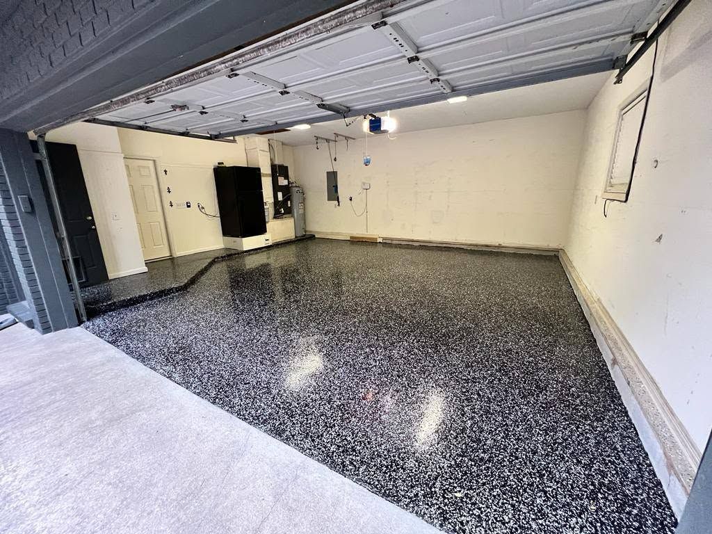 Empty garage with speckled epoxy floor, white walls, and an open overhead door.