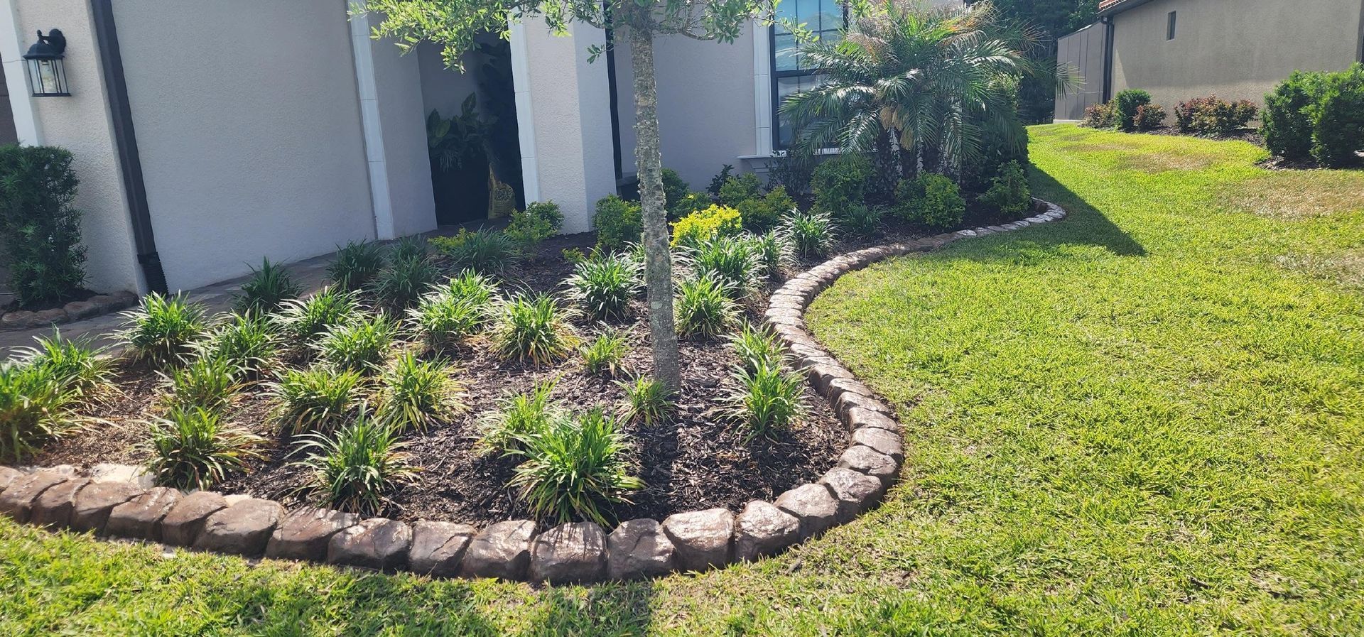 Curved stone border around landscaped mulch bed with shrubs beside a house and green lawn