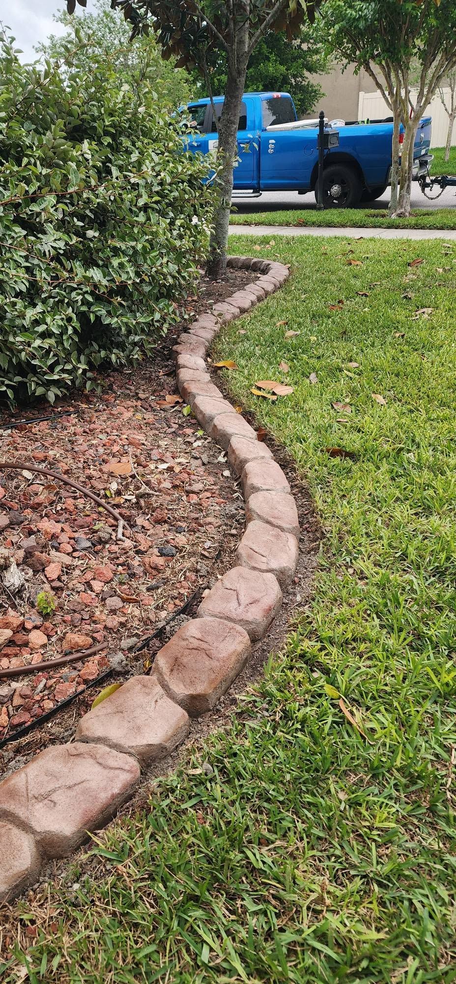 Curved brick garden border edging a grassy lawn, with shrubs and a blue pickup truck in the background