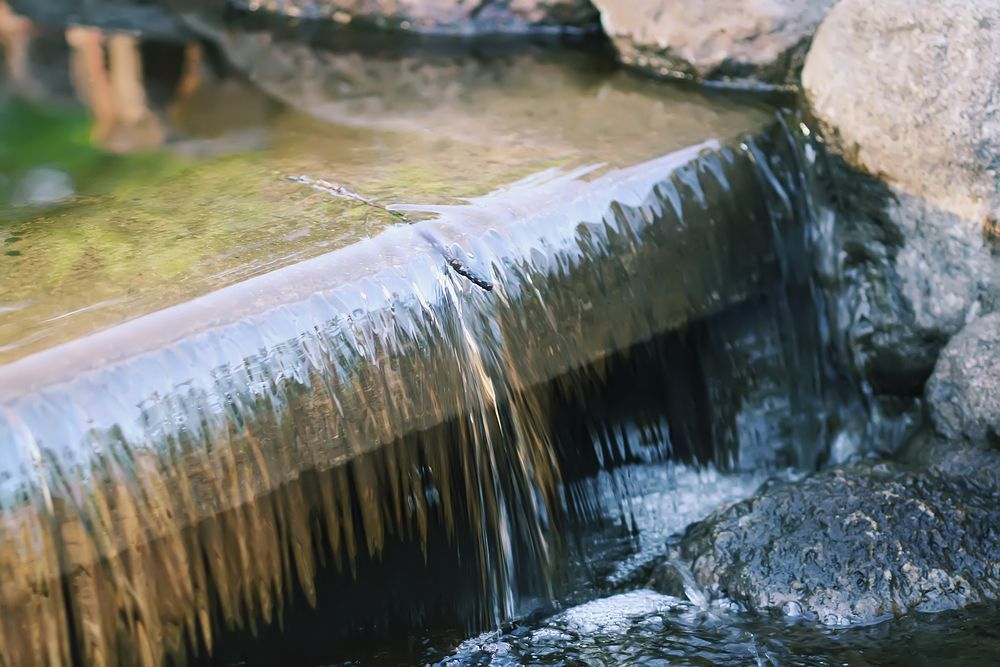 Small waterfall flowing over a stone ledge into a rocky stream
