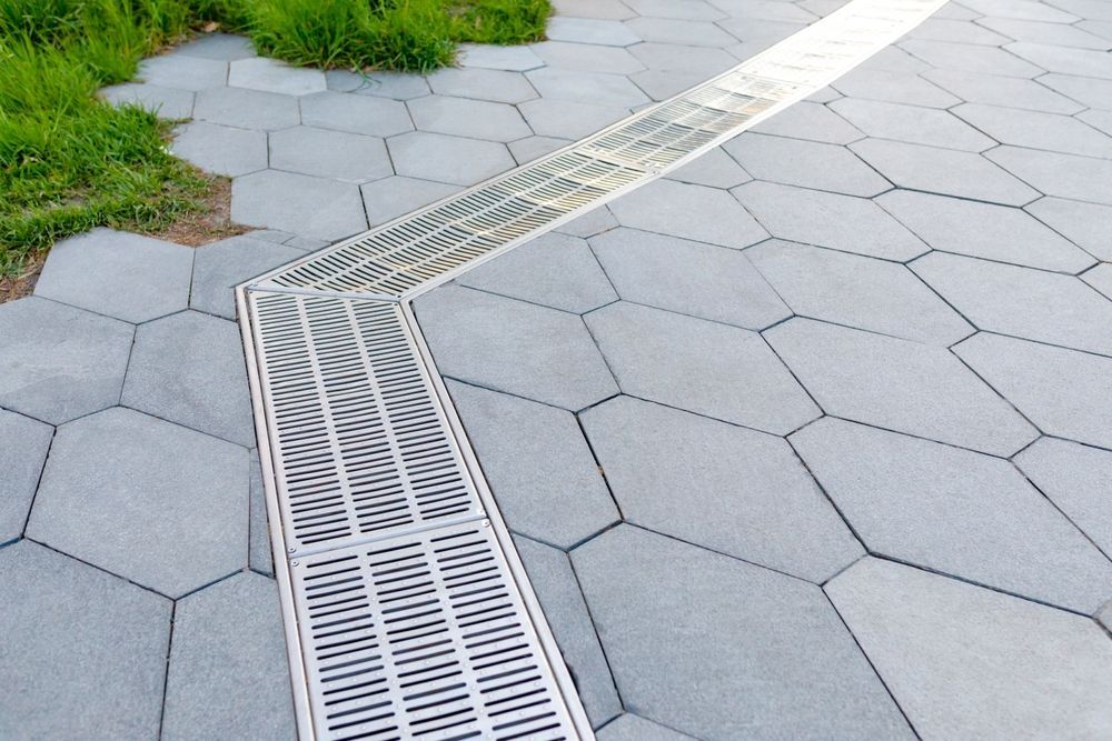 Gray hexagonal pavers with a diagonal metal drain grate beside green grass