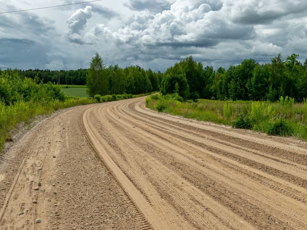 Curving sandy dirt road through green fields under a cloudy sky
