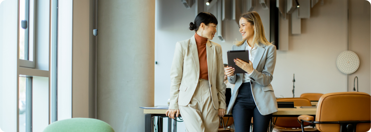 two women in corporate attire holding coffees walking down stairs smiling at each other