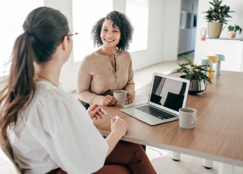 Two people talking in a bright office, one smiling across from another during a meeting
