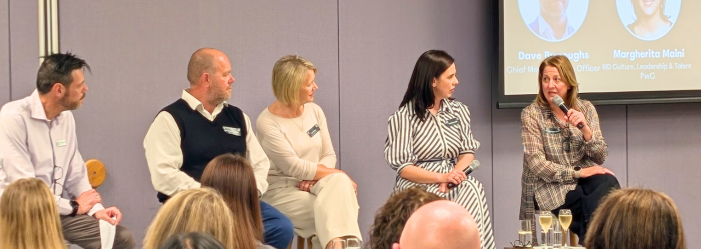 Five people seated on stage for a panel discussion, with a projected slide behind them