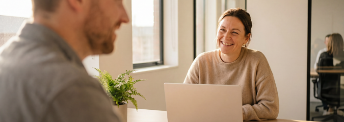HR professional in office at a laptop smiles at a male colleague