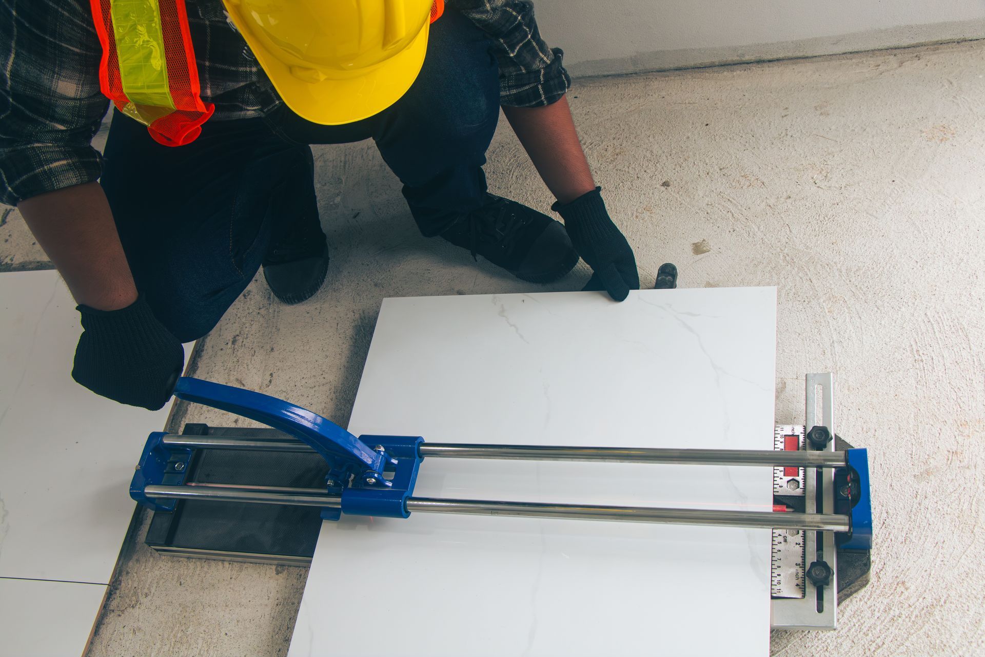 Bathroom remodeling contractor in safety gear cutting white tile with a blue tile cutter