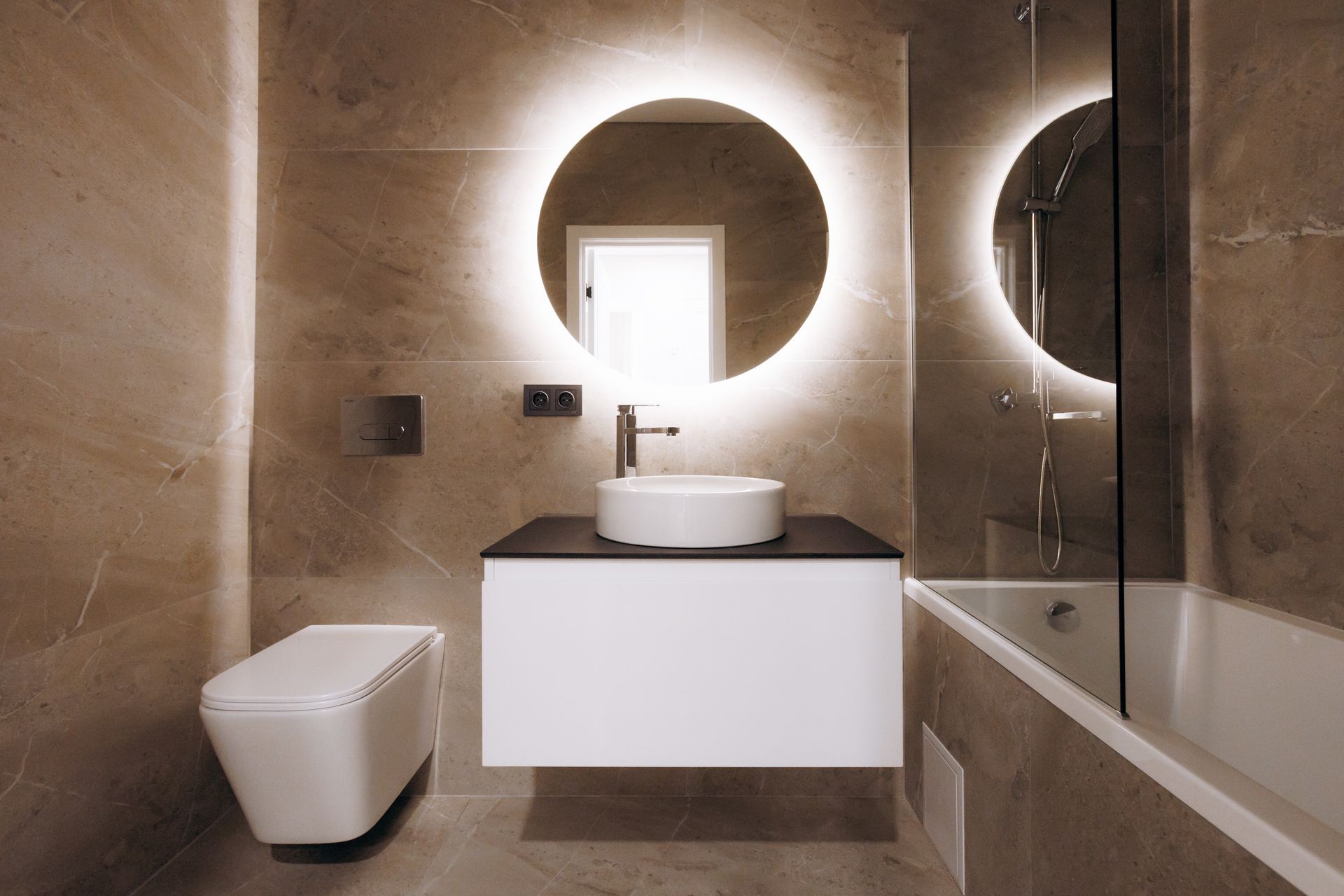 Beige marble bathroom by a bathroom remodeler with backlit round mirror and floating vanity