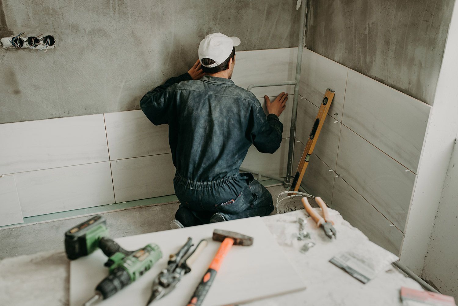 Contractor installing ceramic wall tiles in a bathroom with tools spread on a work surface. Contractor installing ceramic wall tiles in a bathroom with tools spread on a work surface.