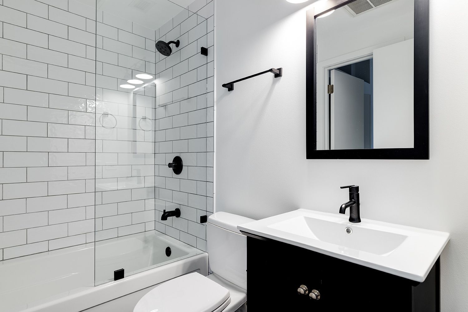 Modern bathroom with subway tile shower, vanity sink, toilet, and black fixtures.