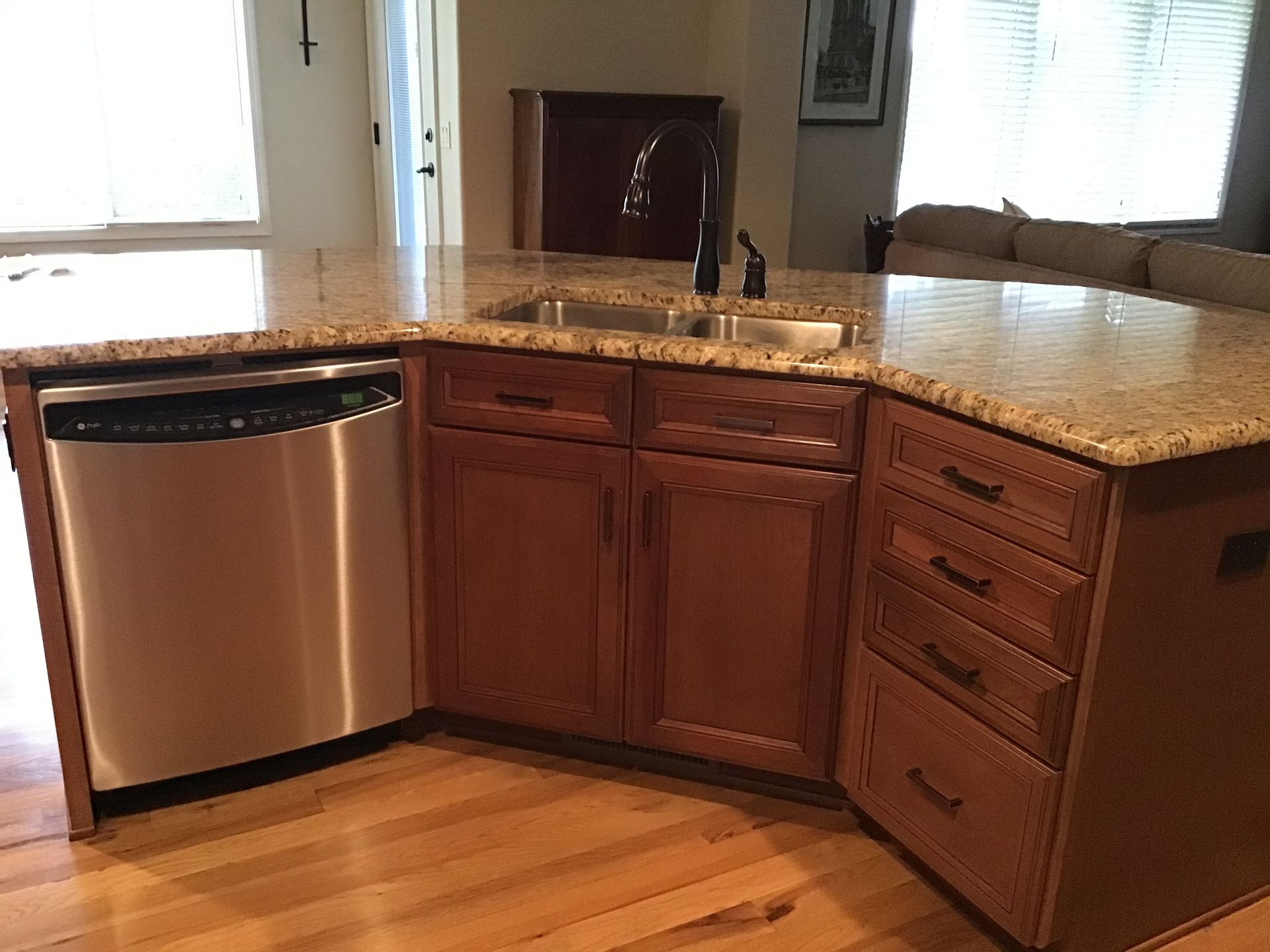 Corner kitchen with stainless dishwasher, wooden cabinets, granite countertop, and hardwood floor