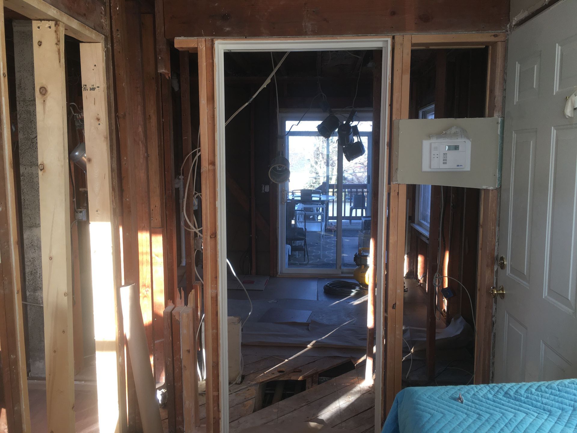 Damaged hallway framing with exposed studs, debris on the floor, and a white panel mounted on the right wall