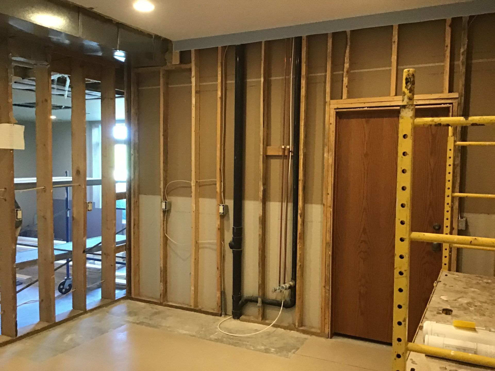 Renovation site with exposed wall studs, insulation, wiring, and a ladder on the right
