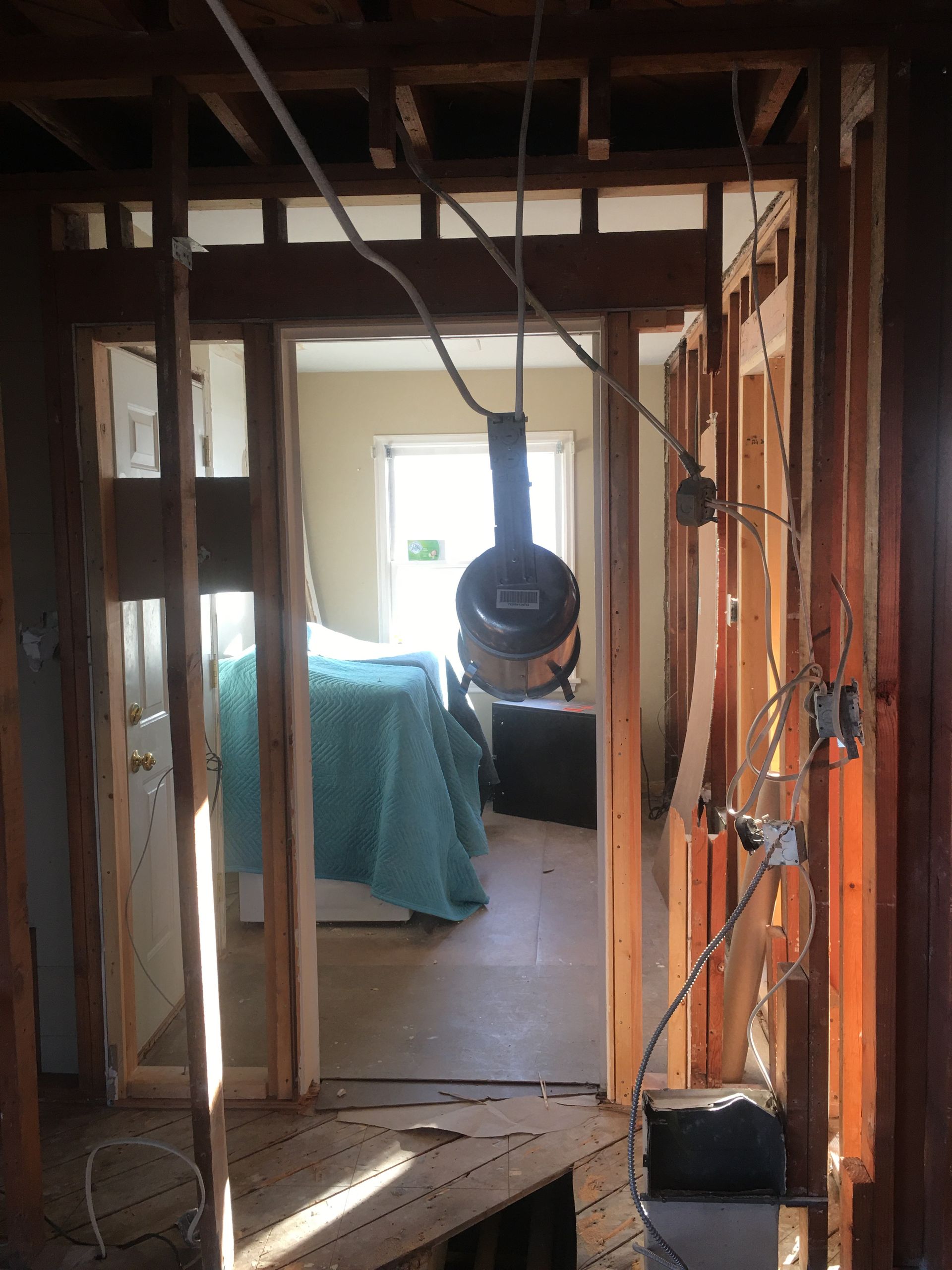 Partially framed room with exposed studs, a hanging fan, and a bed covered in blue in the background