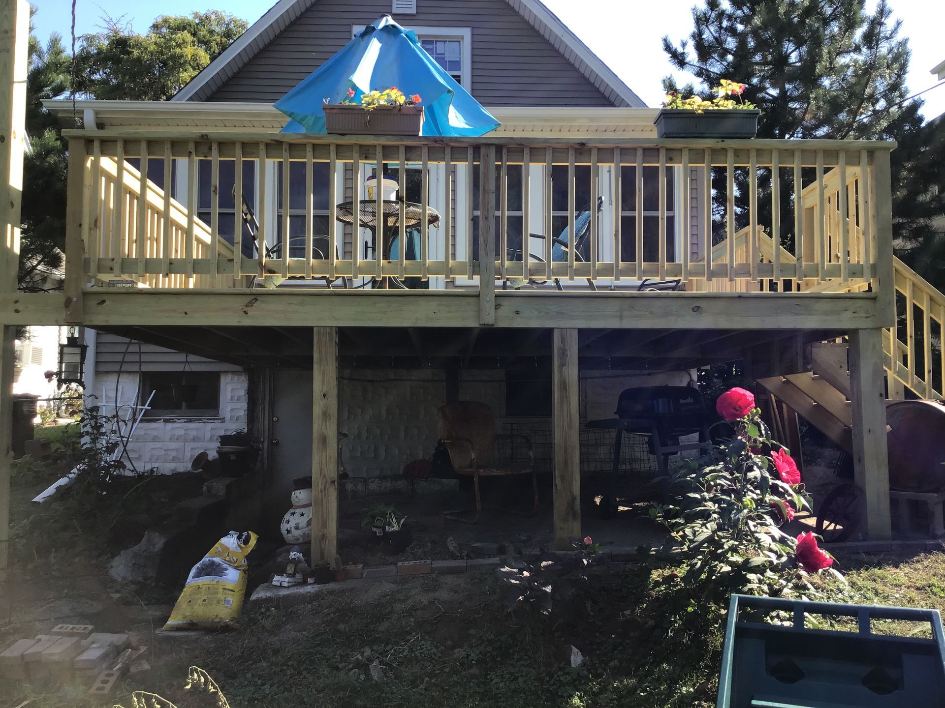 Backyard deck with blue umbrella, stairs, and garden items under a house roofline