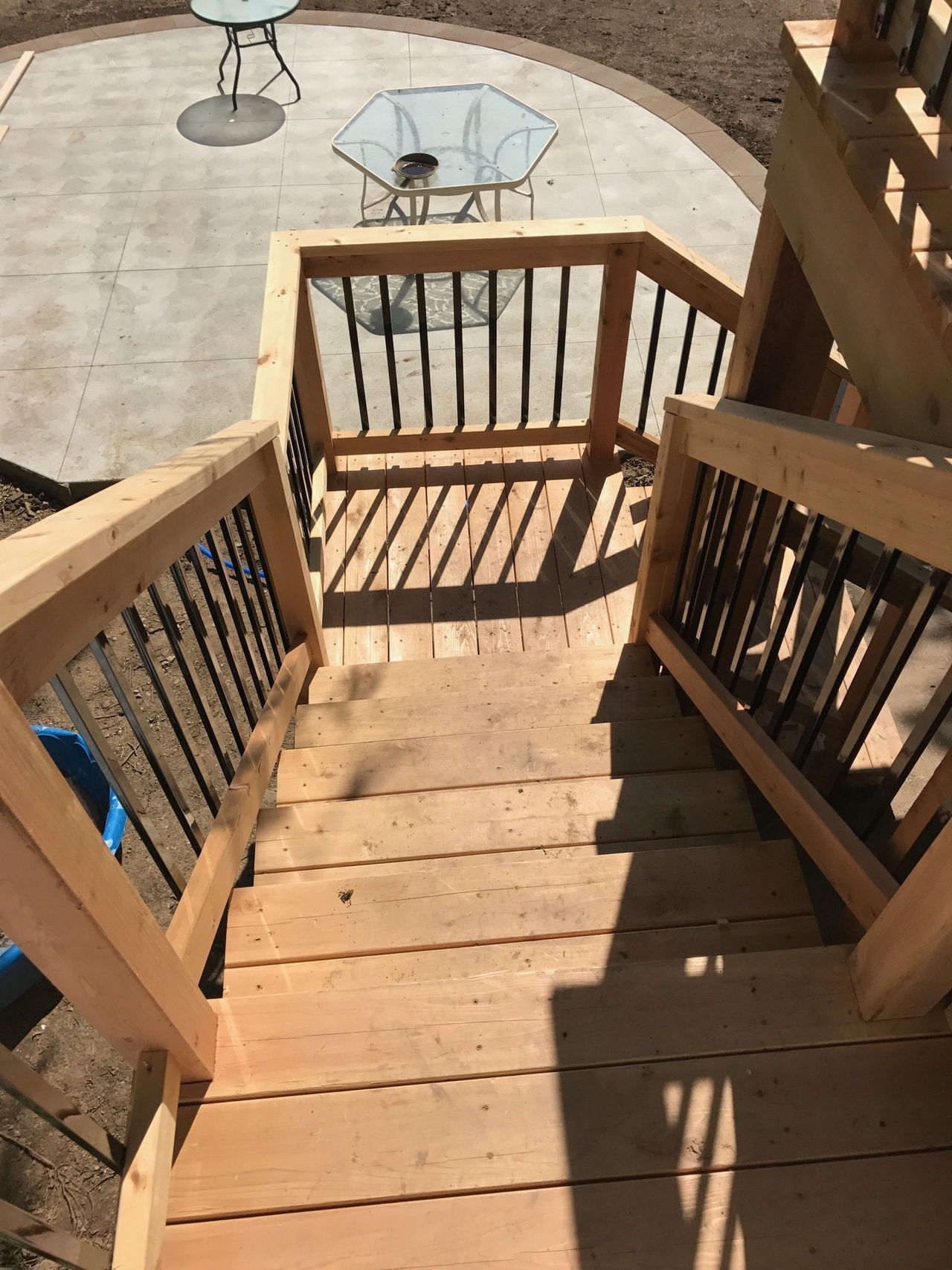 Wooden stairs descending to a patio with a round glass table and chairs in sunlight