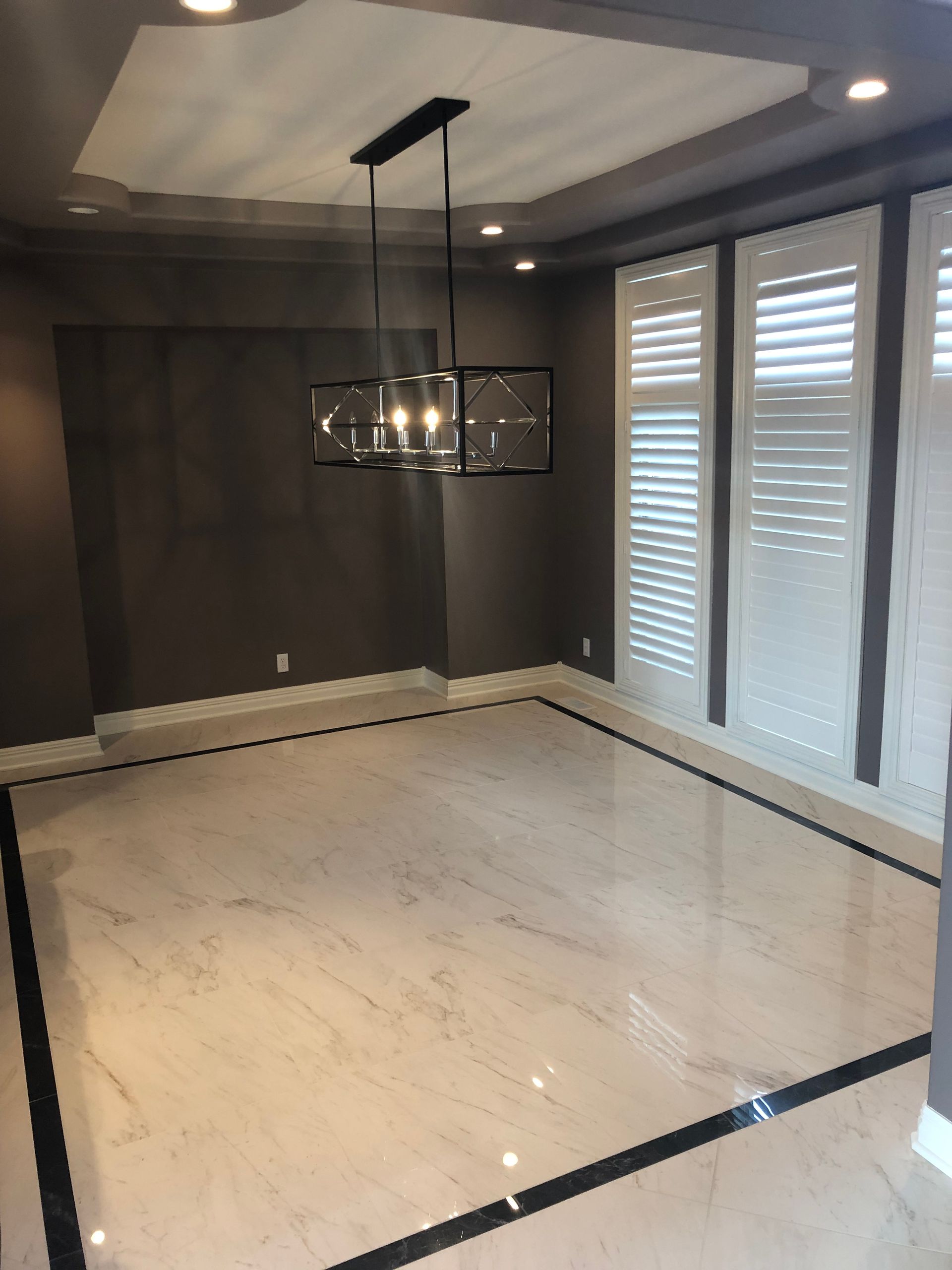 Empty modern dining room with dark walls, white marble floor, chandelier, and large windows with shutters