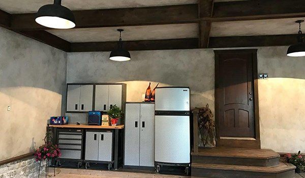 Covered porch with kitchenette cabinets, white fridge, sink, and a brown door against a stucco wall.