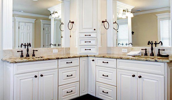Bright white bathroom vanity with double sinks, mirrors, and granite countertop under soft lighting