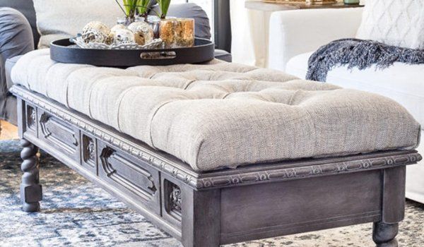 Tufted beige upholstered bench with dark carved wooden legs in a bright living room