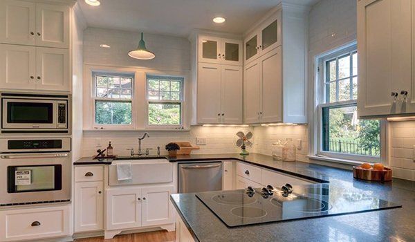 Bright white kitchen with stainless appliances, dark countertops, and a large window over the sink