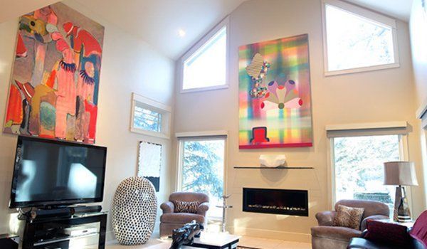 Bright living room with tall windows, fireplace, TV, leather chairs, and colorful abstract wall art