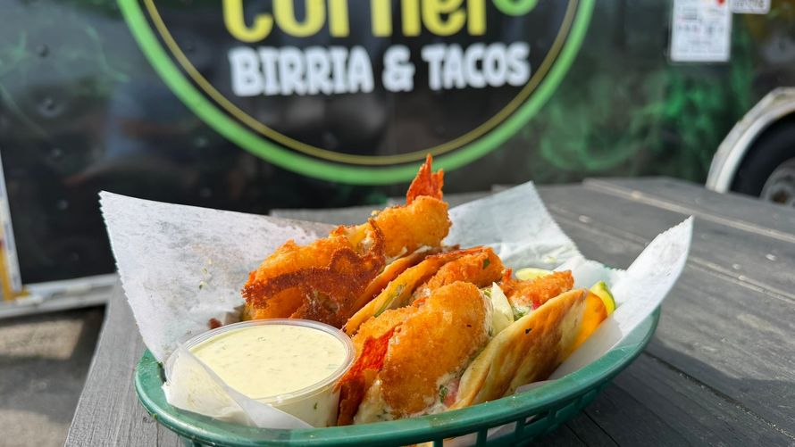 Basket of crispy orange tacos with dipping sauce on a table outside a birria and tacos restaurant
